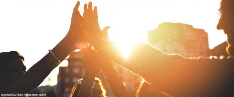 silhouetted group of people high-fiving at sunset with sunglare effect